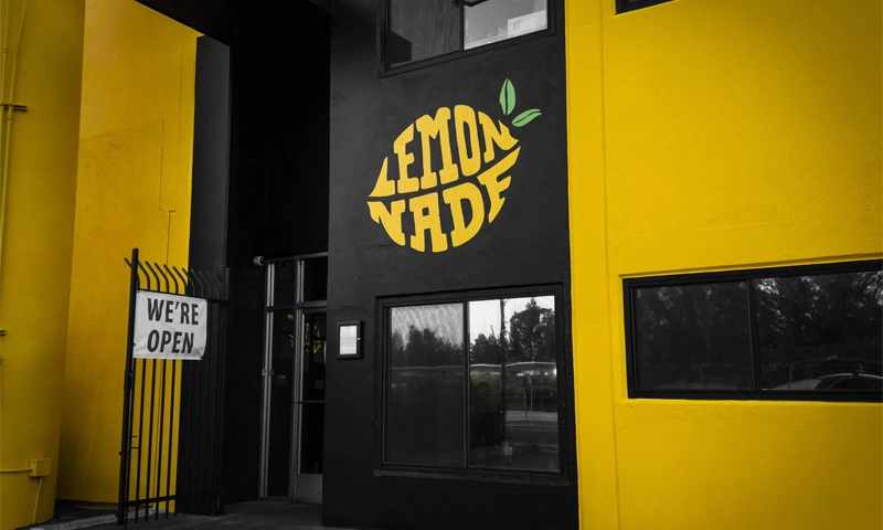 Lemonnade Sacramento - Image of Lemonnade Store front. The store has yellow and black walls on the outside of the store front with the logo above a window.